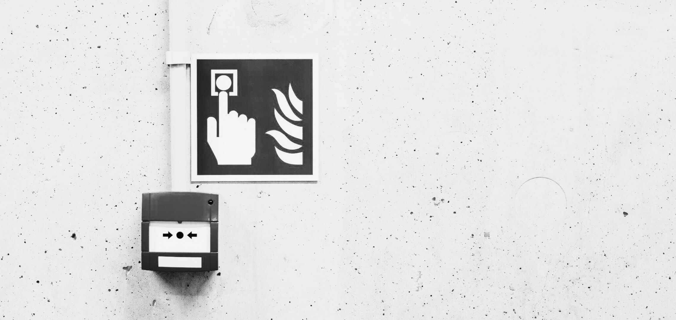 Ein Brandschutzsymbol mit Hand und Flammen ist neben einem Feuermelder an einer weißen Wand zu sehen.